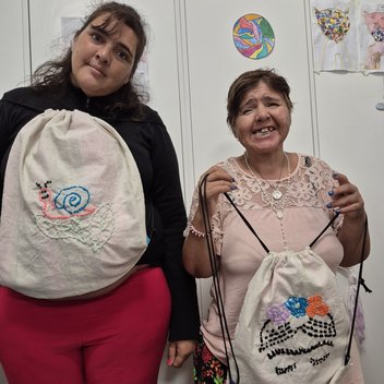 Dos concurrentes de Espacio Encuentro mostrando mochilas bordadas en el taller