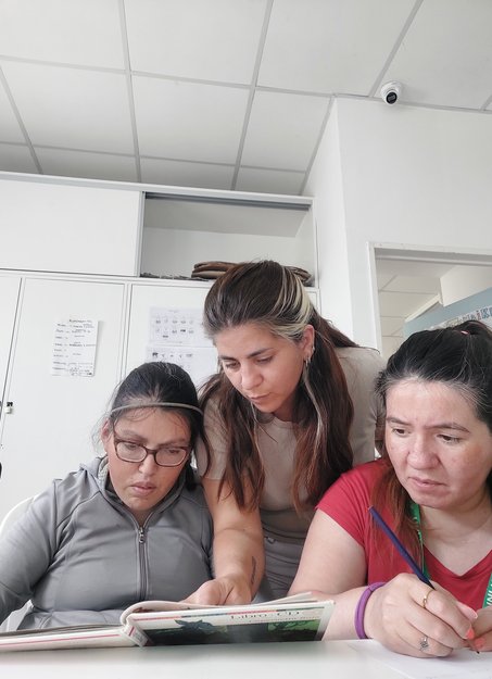 Profesional de Espacio Encuentro acompañando a dos concurrentes en una actividad de lectura
